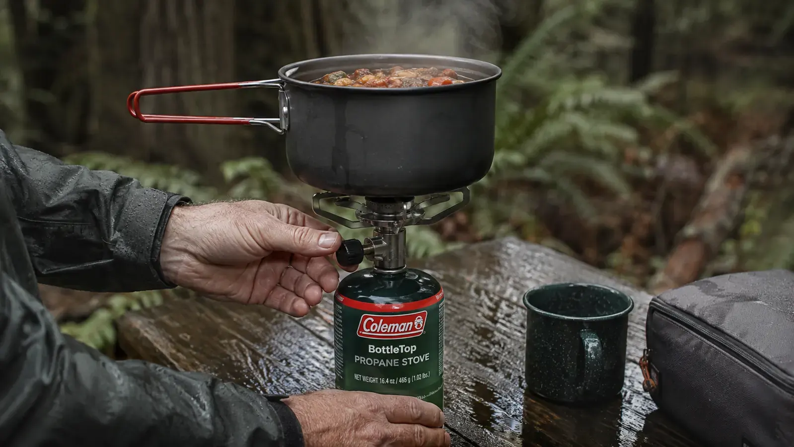 Person's hand turning the control knob on the bottle-top stove while a pot sits on the grate