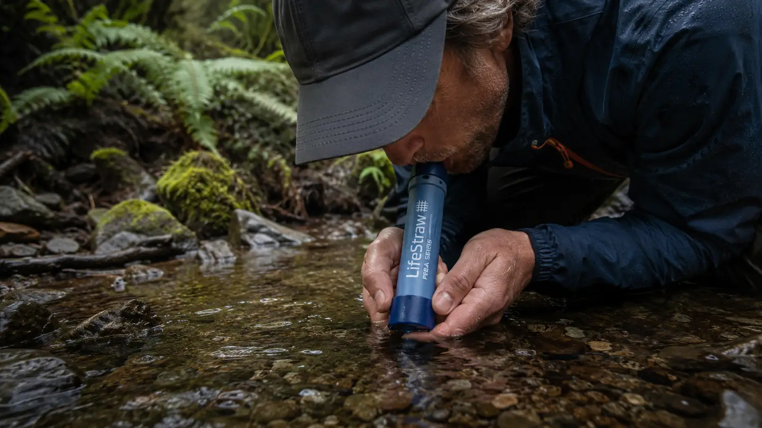 The LifeStraw Peak straw in use, someone drinking directly from a stream, filter visible