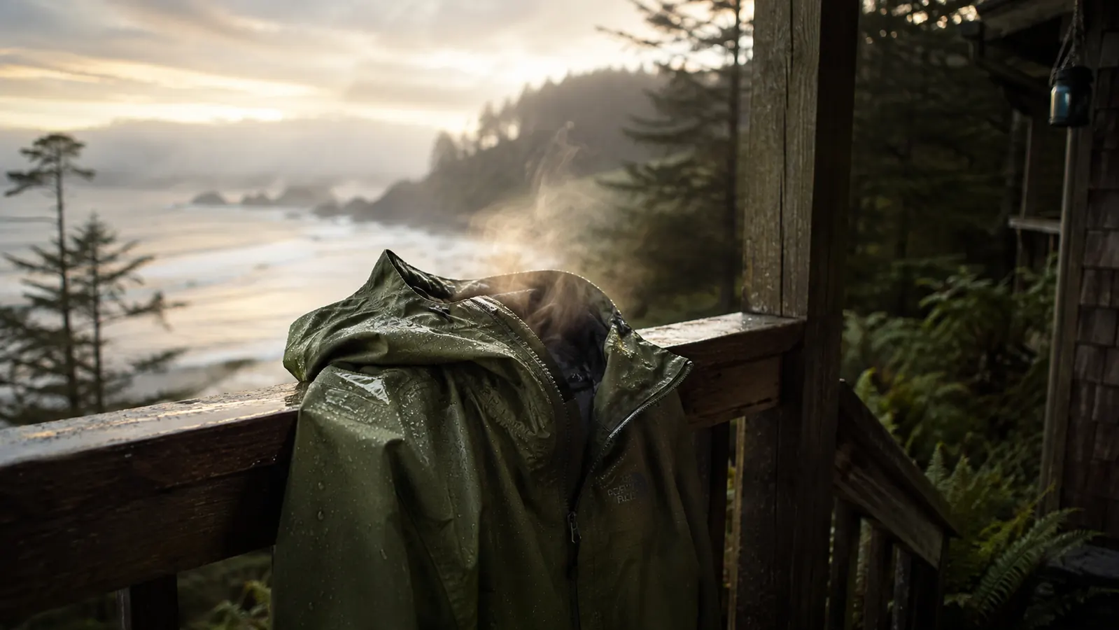 The Marmot Precip Eco hanging to dry on a porch rail at dawn, coast in the background